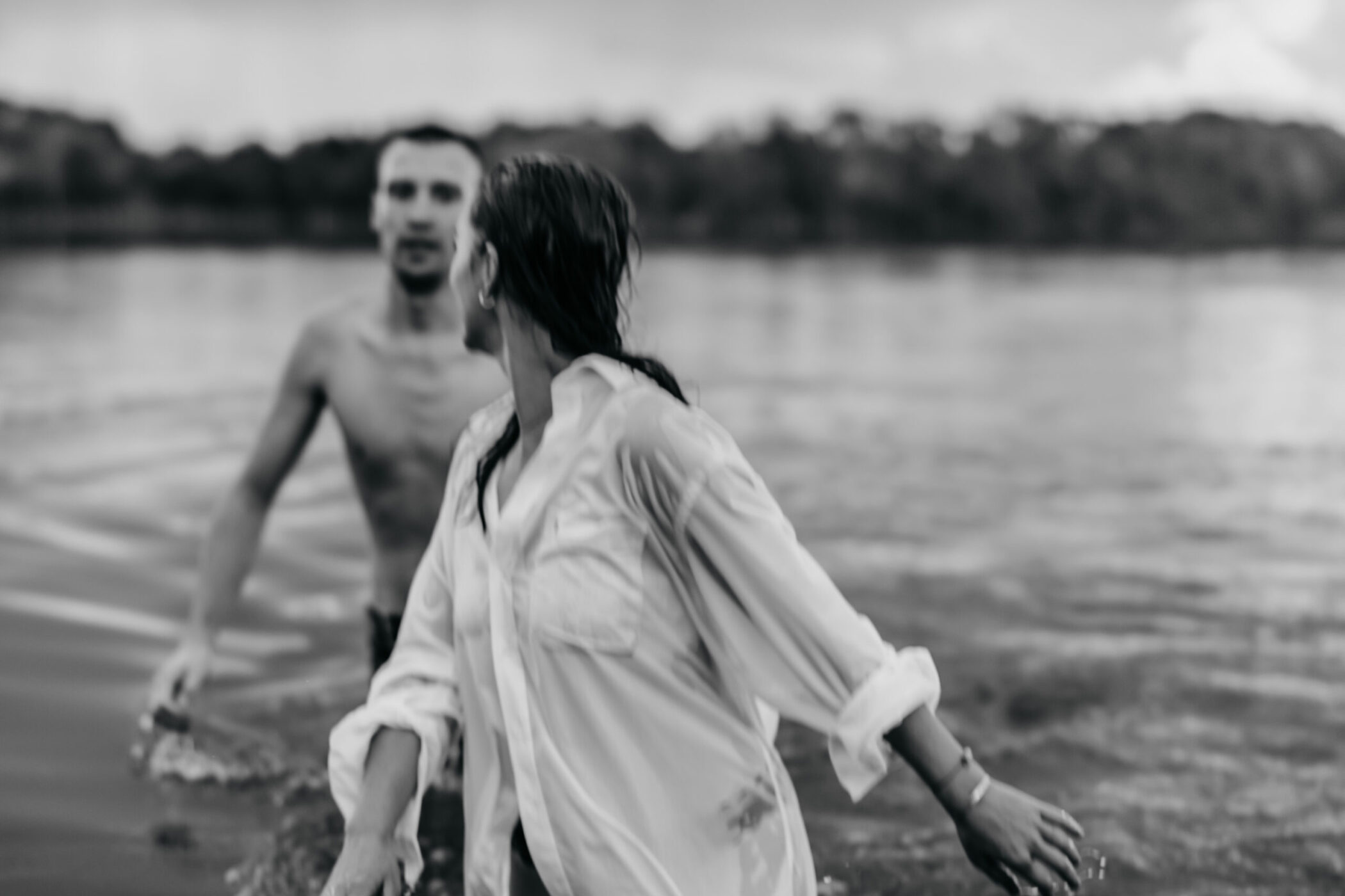 Paar im See, unscharf, Frau blickt zurück auf Mann im Hintergrund.